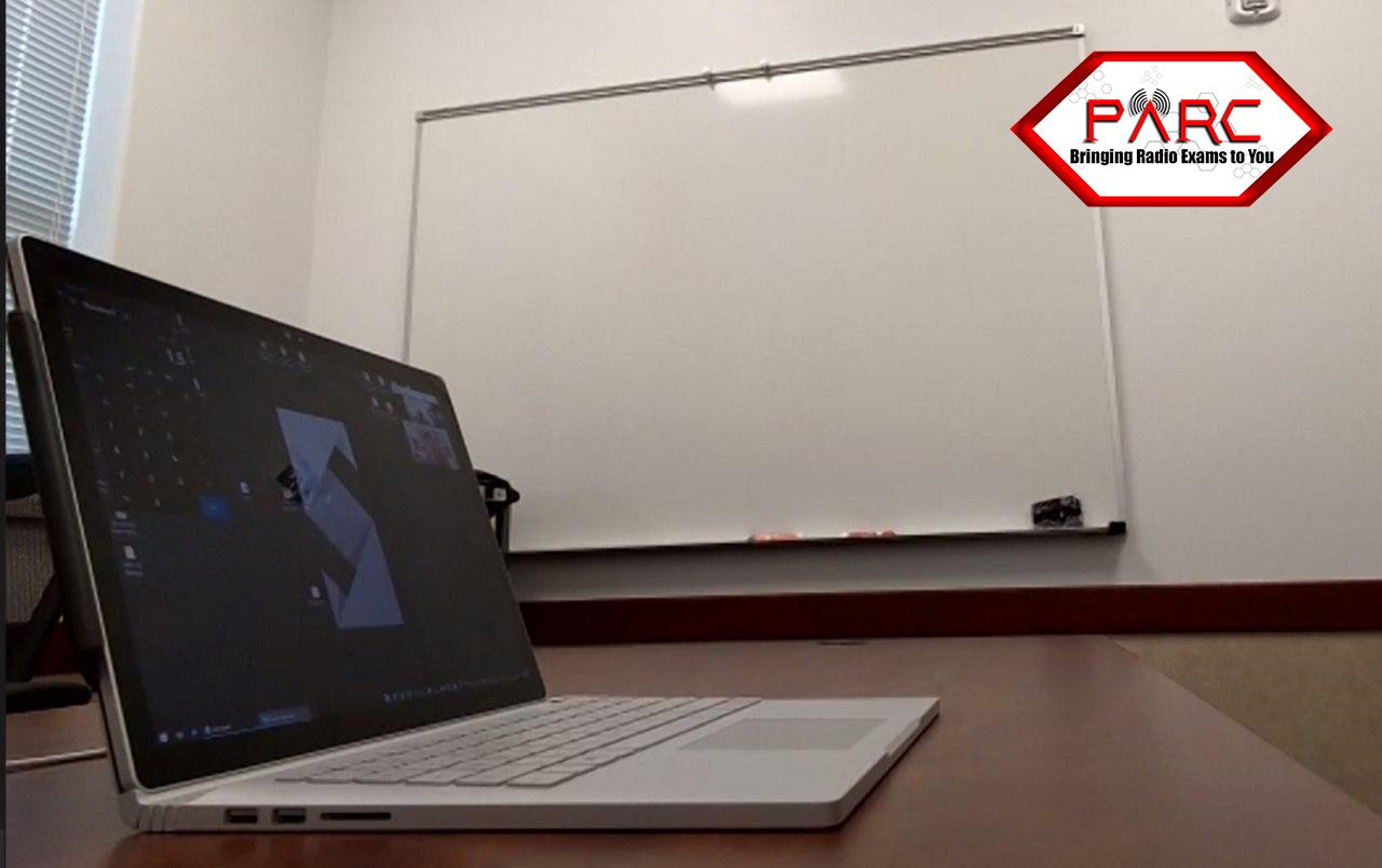 Second-device camera view of a candidate at their desk, showing the keyboard, monitor, and the candidate’s hands from a front and side angle.